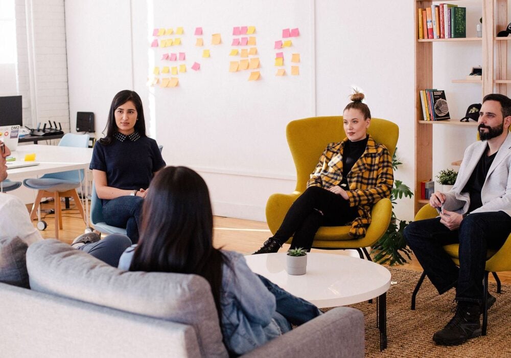 Group of four professionals engaged in a discussion in a modern office setting, with a focus on collaboration and creativity, reflecting Connect Boost Marketing's client-centered approach.