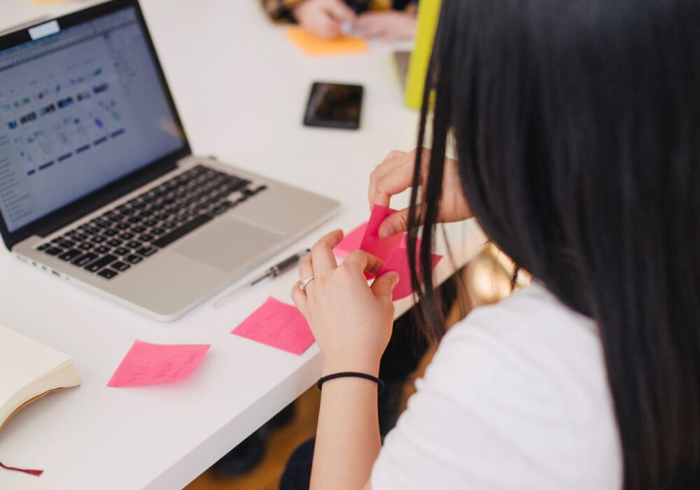 Person working at a desk with a laptop, organizing colorful sticky notes, illustrating brand management and marketing strategy development.